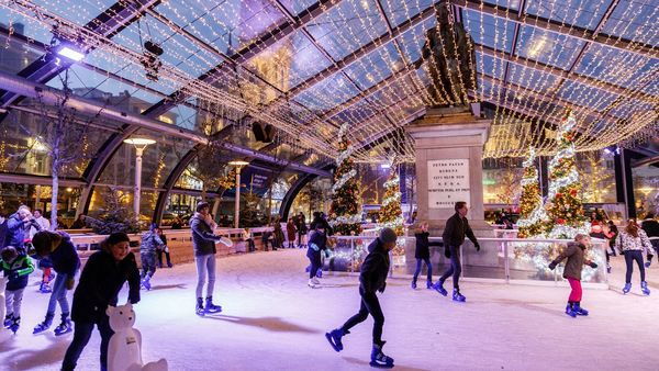 Families and children ice skating under enchanting Christmas lights at Antwerp Christmas Market in Belgium, surrounded by festive decorations, illuminated trees, and vibrant holiday atmosphere.