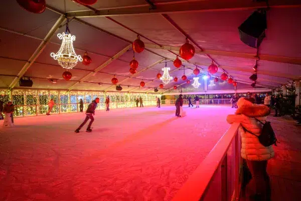 Top 10 Kindvriendelijke Kerstmarkten in Belgiƫ 85 People ice skating at the indoor rink decorated with glowing chandeliers and ornaments at Bruges Christmas Market in Belgium, surrounded by sparkling festive lights and a joyful winter atmosphere.