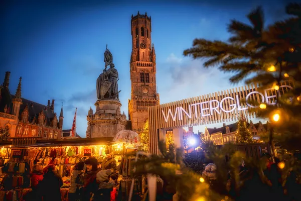 Top 10 Kindvriendelijke Kerstmarkten in Belgiƫ 83 Visitors shopping under golden festive lights at Bruges Christmas Market in Belgium, with the iconic Belfry tower, statue, and sparkling