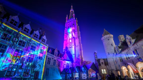 Top 10 Kindvriendelijke Kerstmarkten in Belgiƫ 82 Spectacular Winter Glow light show illuminating the Church of Our Lady and historic buildings at Bruges Christmas Market in Belgium, creating a magical festive atmosphere with vibrant colors and architecture.