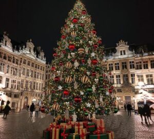 Top 10 Kindvriendelijke Kerstmarkten in Belgiƫ 86 Magnificent Christmas tree adorned with red, green and gold ornaments surrounded by colorful gift boxes at Grand Place, Brussels Christmas Market in Belgium, with stunning illuminated historic buildings at night.