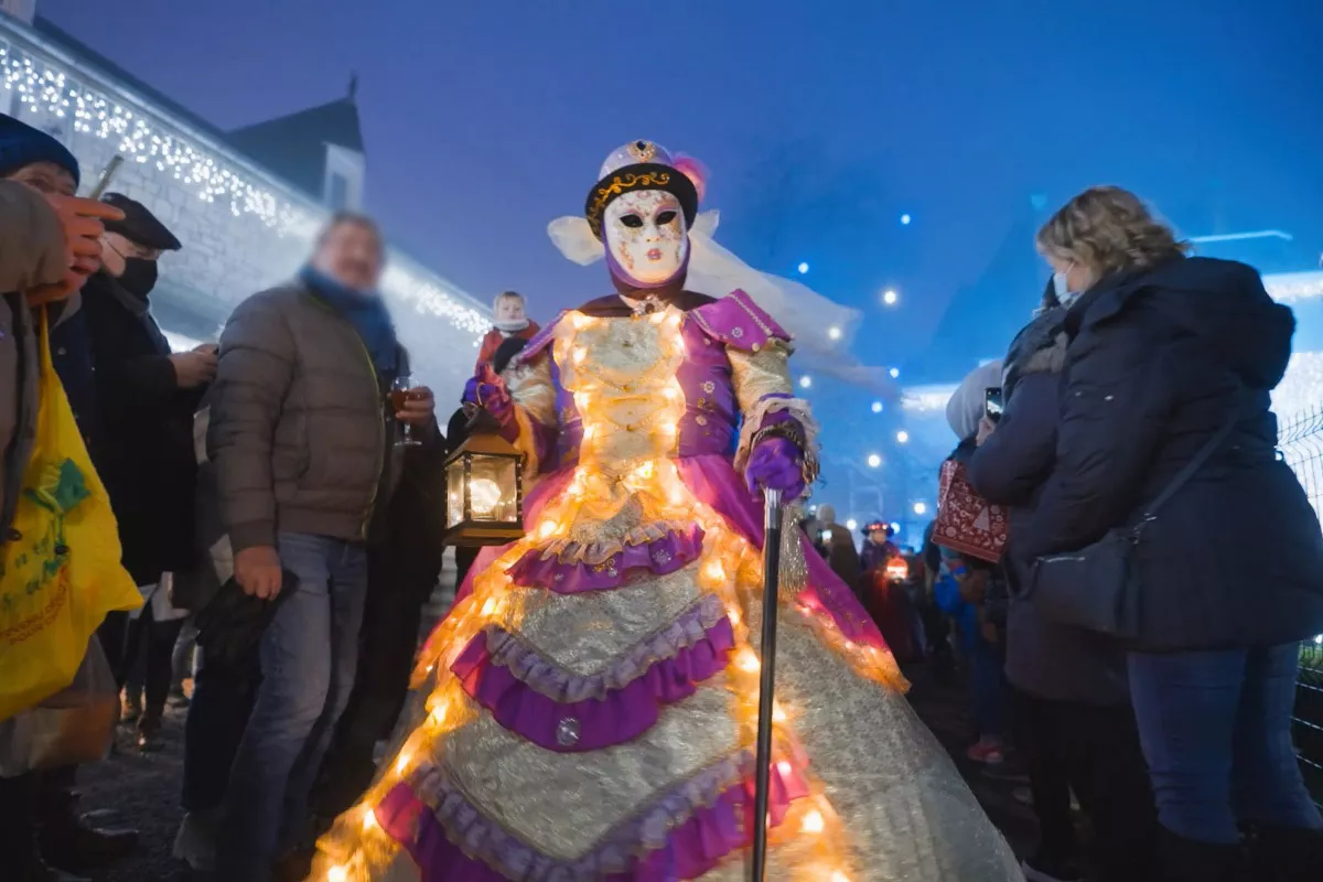 Top 10 Best Child-Friendly Christmas Markets in Belgium 73 Performer in a glowing, ornate purple and white illuminated dress leading a festive costume parade at Ciney Christmas Market in Germany, surrounded by visitors enjoying the vibrant Christmas celebration.