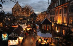 Colmar Christmas Market glowing with festive lights and bustling holiday stalls, as families explore charming Alsace streets under illuminated winter trees at dusk. A top travel destination for magical holiday and family experiences in France.