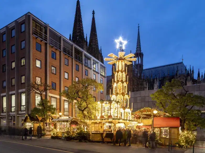 Top 10 Kindvriendelijke Kerstmarkten in Duitsland 45 Experience the festive magic of Christmas in Cologne with the glowing holiday pyramid and iconic cathedral spires as a backdrop. This enchanting evening scene highlights sparkling market lights, cheerful visitors, and the unique holiday atmosphere in Cologne’s vibrant city center.