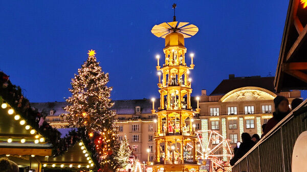 Experience the enchanting Dresden Striezelmarkt with its iconic glowing Christmas pyramid and festive tree against a historic city backdrop. This magical evening scene captures twinkling holiday lights, cheerful crowds, and the rich traditions of Germany’s oldest Christmas market.