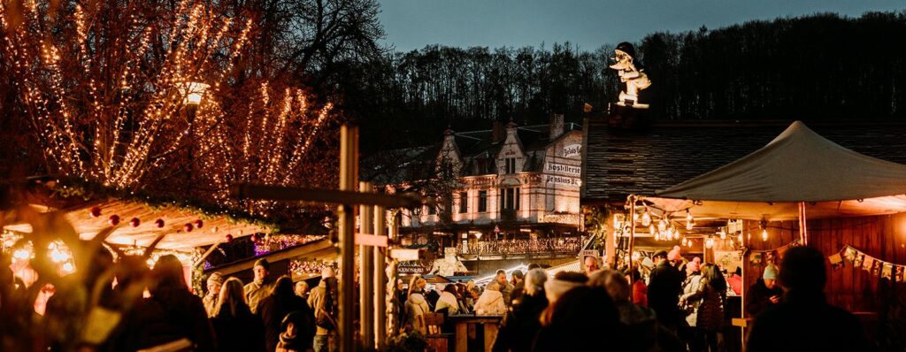 Top 10 Kindvriendelijke Kerstmarkten in Belgiƫ 103 Visitors gather under sparkling lights at rustic wooden stalls in the historic center of Durbuy Christmas Market in Belgium, with glowing trees and charming old buildings creating a magical festive atmosphere.
