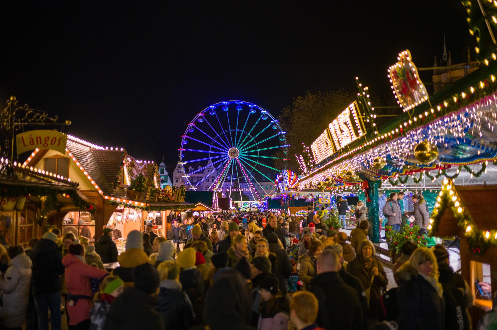 Experience the festive energy of Erfurt Weihnachtsmarkt with vibrant holiday crowds, twinkling market stalls, and the iconic illuminated Ferris wheel. This lively night scene captures joyful visitors, colorful lights, and the magical atmosphere of one of Germany’s top Christmas markets.