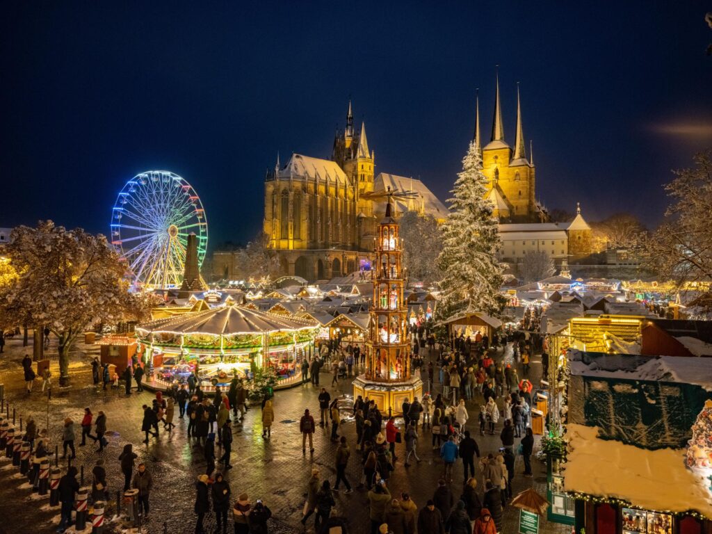 Experience the enchanting Erfurt Weihnachtsmarkt with its sparkling cathedral backdrop, twinkling Ferris wheel, and bustling holiday crowds. This magical night scene showcases festive stalls, illuminated towers, and joyful visitors at one of Germany’s most beautiful Christmas markets.