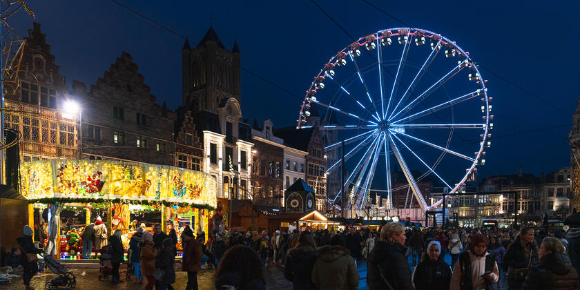 Top 10 Kindvriendelijke Kerstmarkten in Belgiƫ 81 Crowds enjoying festive attractions at Ghent Christmas Market in Belgium, featuring a brightly lit Ferris wheel, illuminated nativity display, and stunning historic buildings in the city center at night.