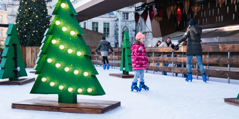 Children and adults ice skating among illuminated Christmas tree decorations at Ghent Christmas Market in Belgium, creating a joyful winter scene with holiday spirit in a lively city square.