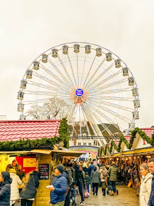 Crowds of families and visitors enjoying festive market stalls beneath the iconic Ferris wheel at Maastricht Magical Christmas Market. Lively holiday atmosphere in the Netherlands featuring local food, crafts, and seasonal decorations in Vrijthof Square.