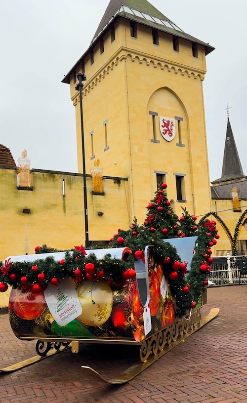 Outdoor Christmas sleigh decorated with ornaments and garlands in front of Valkenburg castle tower, showcasing the festive entrance to Valkenburg Christmas Markets in the Netherlands. A popular family-friendly winter destination known for unique holiday events and sparkling decorations.