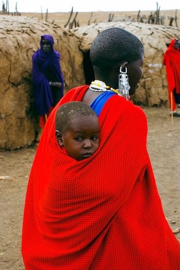 Maasai moeder draagt haar kind op de rug in een rode doek in Tanzania – warm portret van het gezinsleven binnen de Maasai gemeenschap.