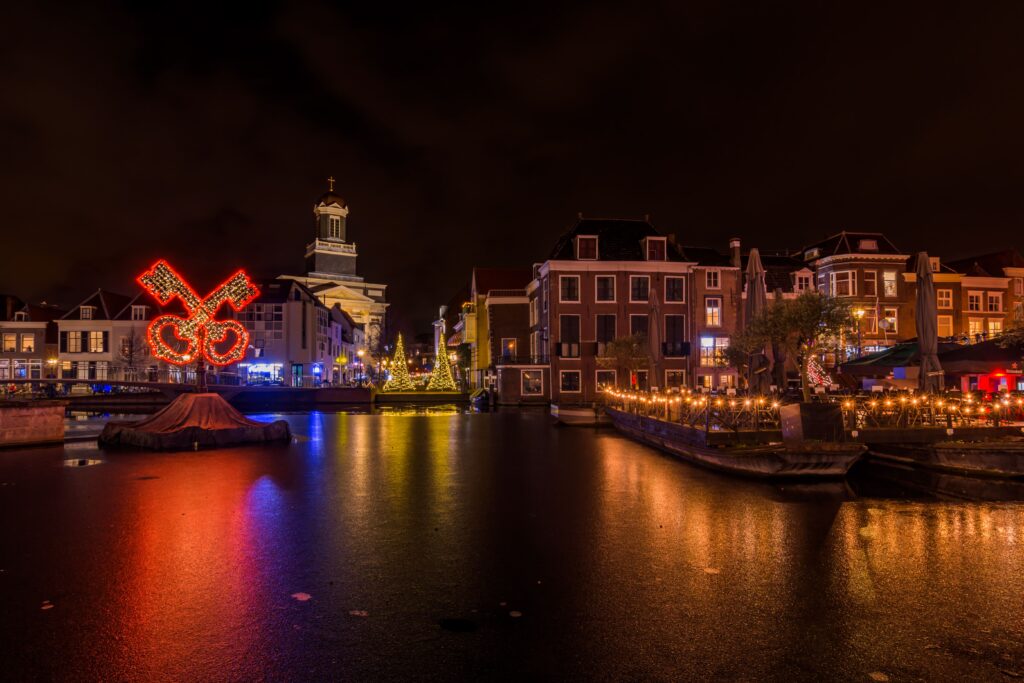 Night photo of the Leiden Floating Christmas Market, showing illuminated canals, decorated Christmas trees, and historic Dutch buildings. Family-friendly holiday atmosphere with festive lights reflecting on the water in the heart of Leiden, Netherlands.
