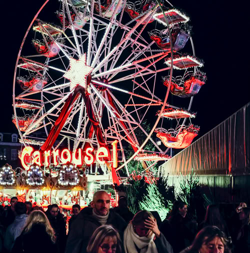 Top 10 Kindvriendelijke Kerstmarkten in Belgiƫ 99 Vibrant night scene at Leuven Christmas Market in Belgium with a brightly lit Ferris wheel, cheerful crowds, and festive carrousel rides, creating a magical holiday atmosphere in the city center.