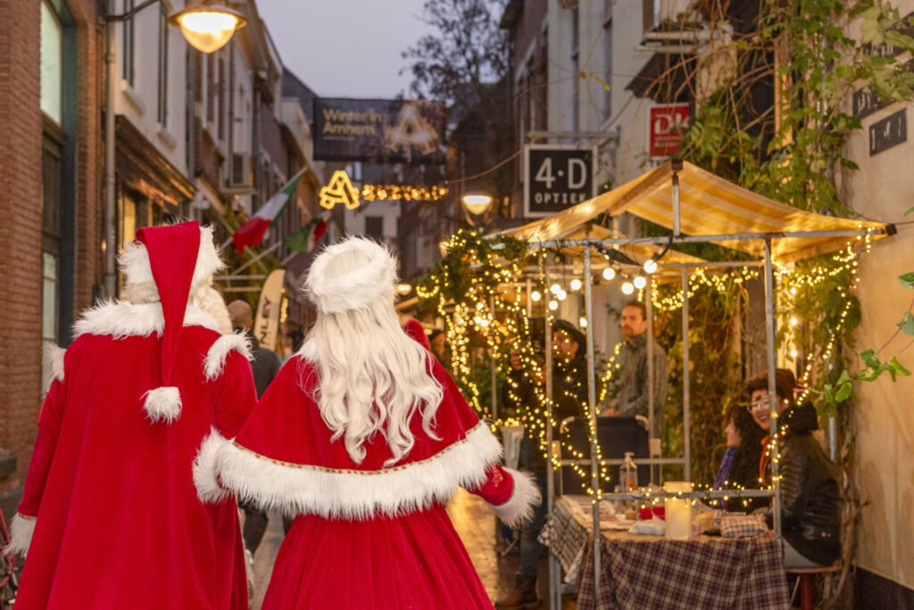 Santa and Mrs. Claus stroll through a beautifully decorated street at Winter in Arnhem Christmas Market. Twinkling holiday lights, festive stalls, and cozy outdoor atmosphere welcome families to enjoy seasonal celebrations in Arnhem, Netherlands.