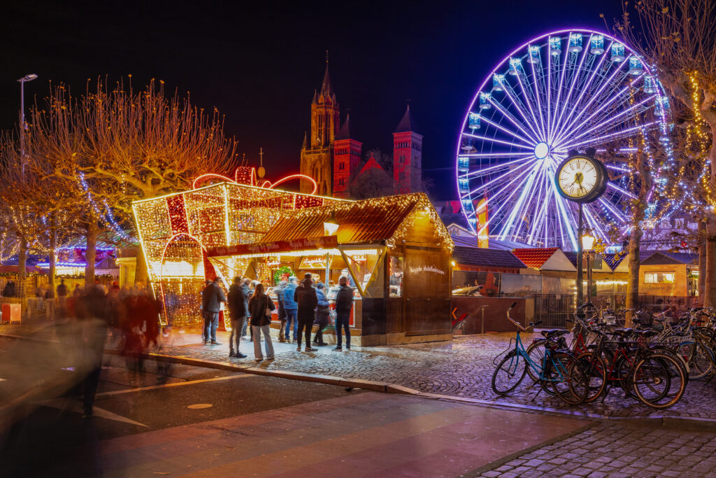 Top 10 Kindvriendelijke Kerstmarkten in Nederland 24 Illuminated holiday stalls and a glowing Ferris wheel at Maastricht Magical Christmas Market, with St. Servatius Basilica in the background. Vibrant family-friendly winter destination in the Netherlands, featuring festive lights, market attractions, and seasonal cheer.