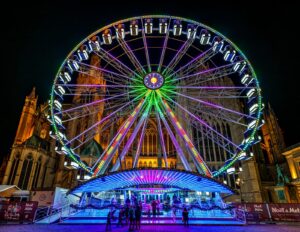 Spectacular illuminated Ferris wheel in front of Metz Cathedral at Metz Christmas Market, France. Families and visitors enjoy vibrant holiday lights and festive atmosphere under the night sky in Lorraine region.