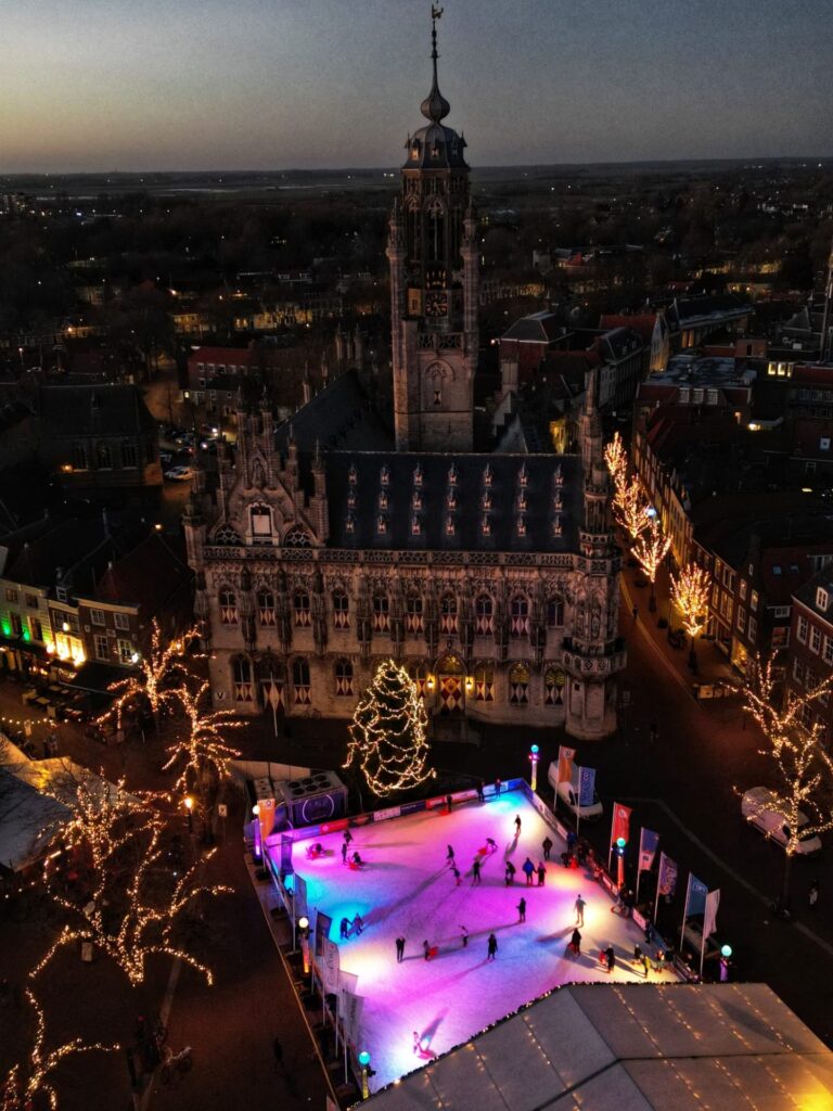 Aerial view of families ice skating at Middelburg Winter Market, surrounded by sparkling holiday lights and the beautifully lit historic town hall. Cozy Christmas atmosphere, festive decorations, and winter activities in Middelburg, Netherlands.