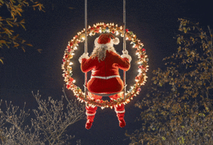 Santa Claus figure sitting on a glowing wreath swing high above the trees at Nantes Christmas Market, creating a whimsical illuminated Christmas decoration that delights families during festive winter evenings in western France.