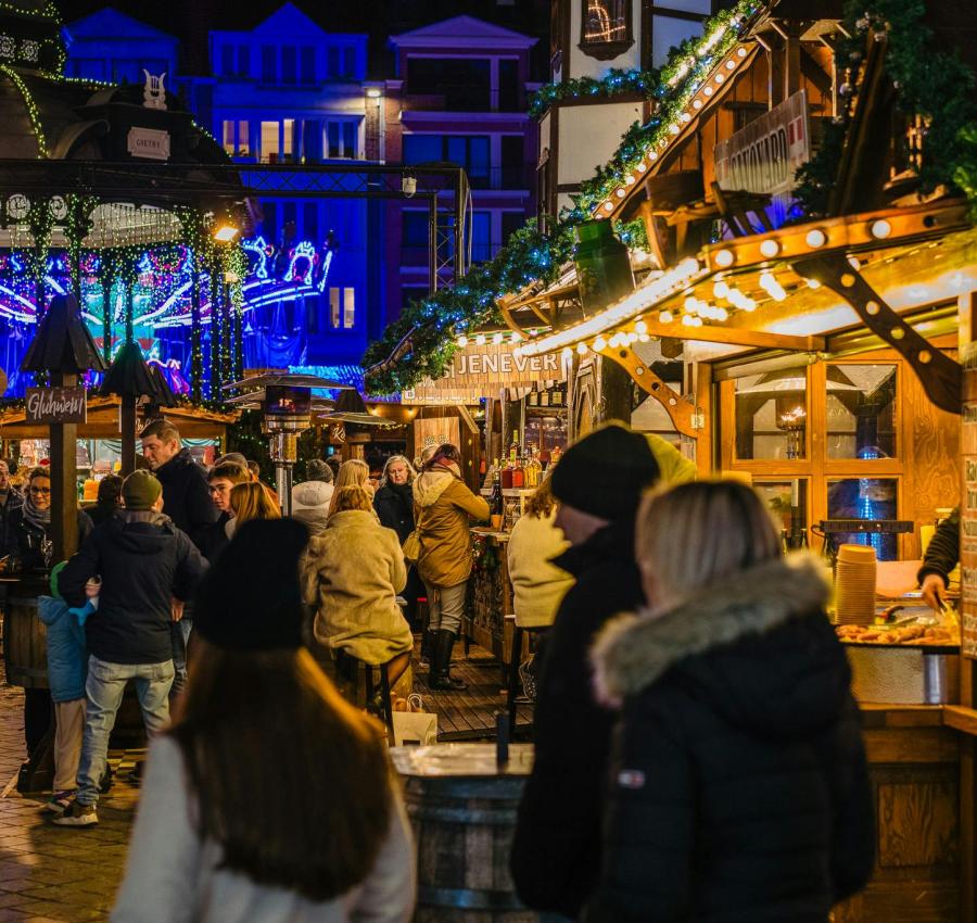 Visitors enjoy holiday treats and drinks at the cozy wooden stalls, illuminated by sparkling lights and festive garlands, during Belgium’s Ostend Christmas Market vibrant night celebrations.