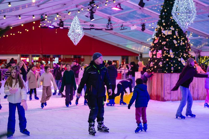 Families and children enjoy ice skating at the festively decorated indoor rink, with a beautiful Christmas tree centerpiece, sparkling lights, and a lively holiday atmosphere at Ostend Christmas Market in Belgium.