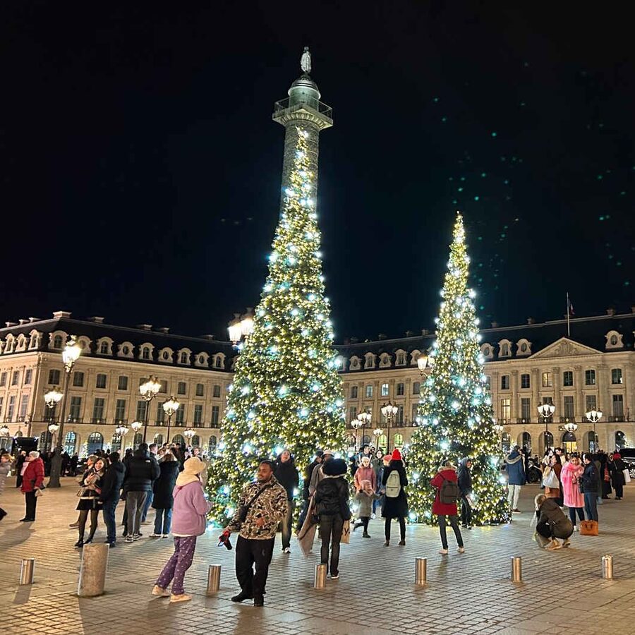 Crowds enjoying sparkling Christmas trees and festive lights at Place Vendôme during Paris Christmas Market, with elegant historic buildings illuminated at night. A magical winter holiday location perfect for family visits and seasonal travel in Paris, France.