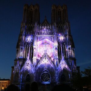 Spectacular Regalia light show illuminating Reims Cathedral’s facade during the Christmas Market at night, with vibrant purple and blue lights creating a magical holiday atmosphere in Champagne, France.