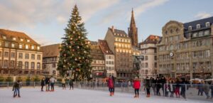 Families and children skating at the festive ice rink in Place Kléber, Strasbourg Christmas Market, with a giant decorated Christmas tree and historic Alsace buildings at sunset. A joyful holiday destination for winter travel and family-friendly experiences in France.