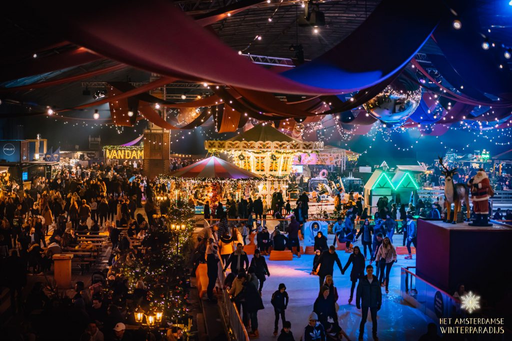 Families and visitors enjoy ice skating, carousel rides, and illuminated market stalls at Amsterdam Winter Paradise Christmas Market indoors. Festive holiday event at RAI Amsterdam with winter activities, sparkling lights, and family-friendly attractions in the Netherlands.